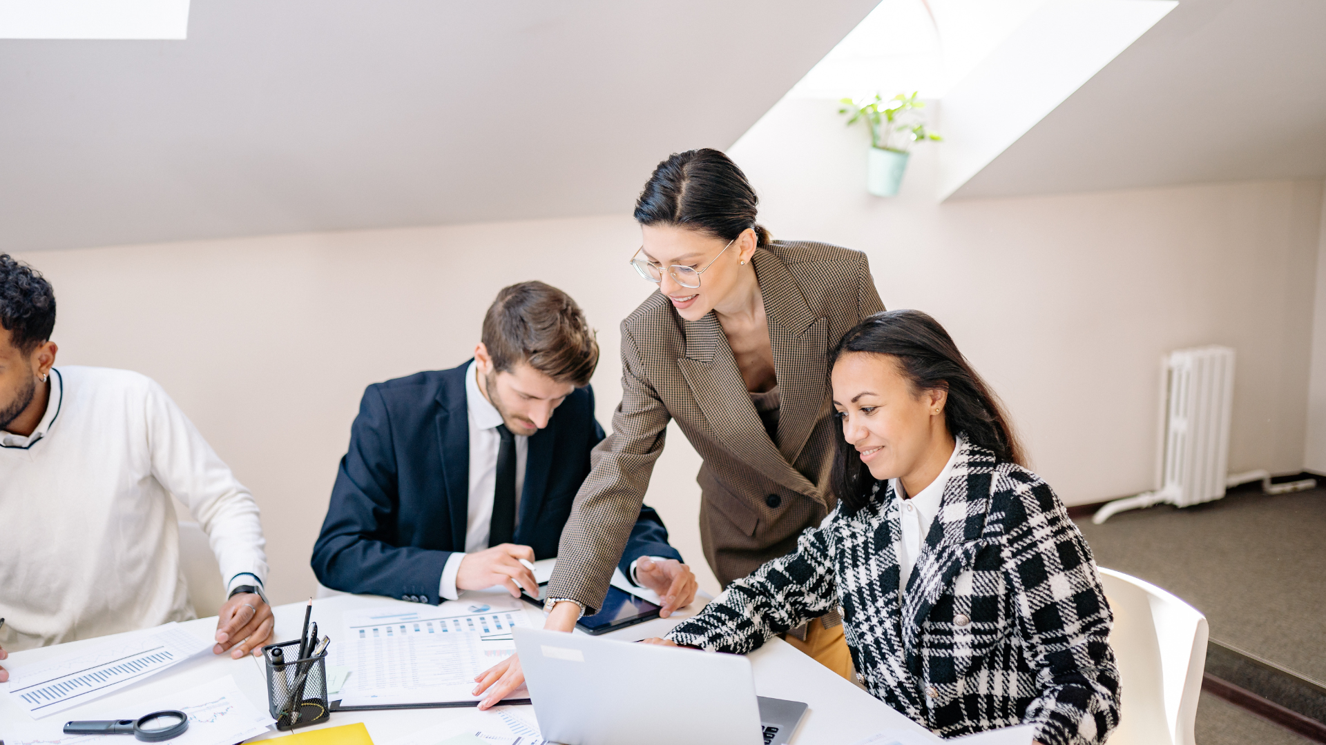 Team reviewing documents at a table; woman in blazer points, others look on.