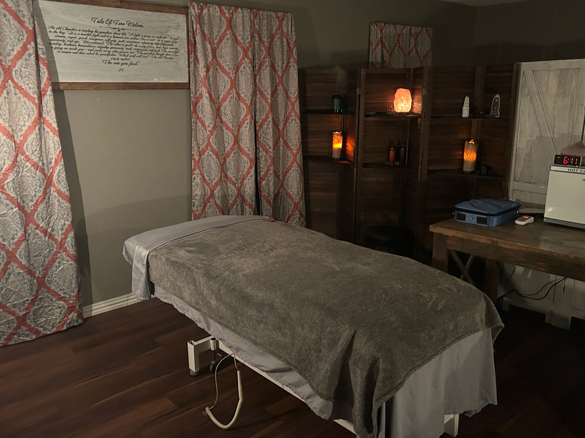 Massage room with massage table, curtains, shelves, and soft lighting.
