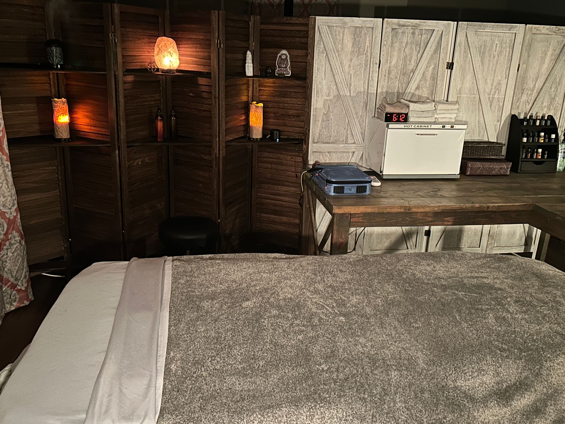 Massage therapy room with massage table, wooden privacy screen, and ambient lighting.
