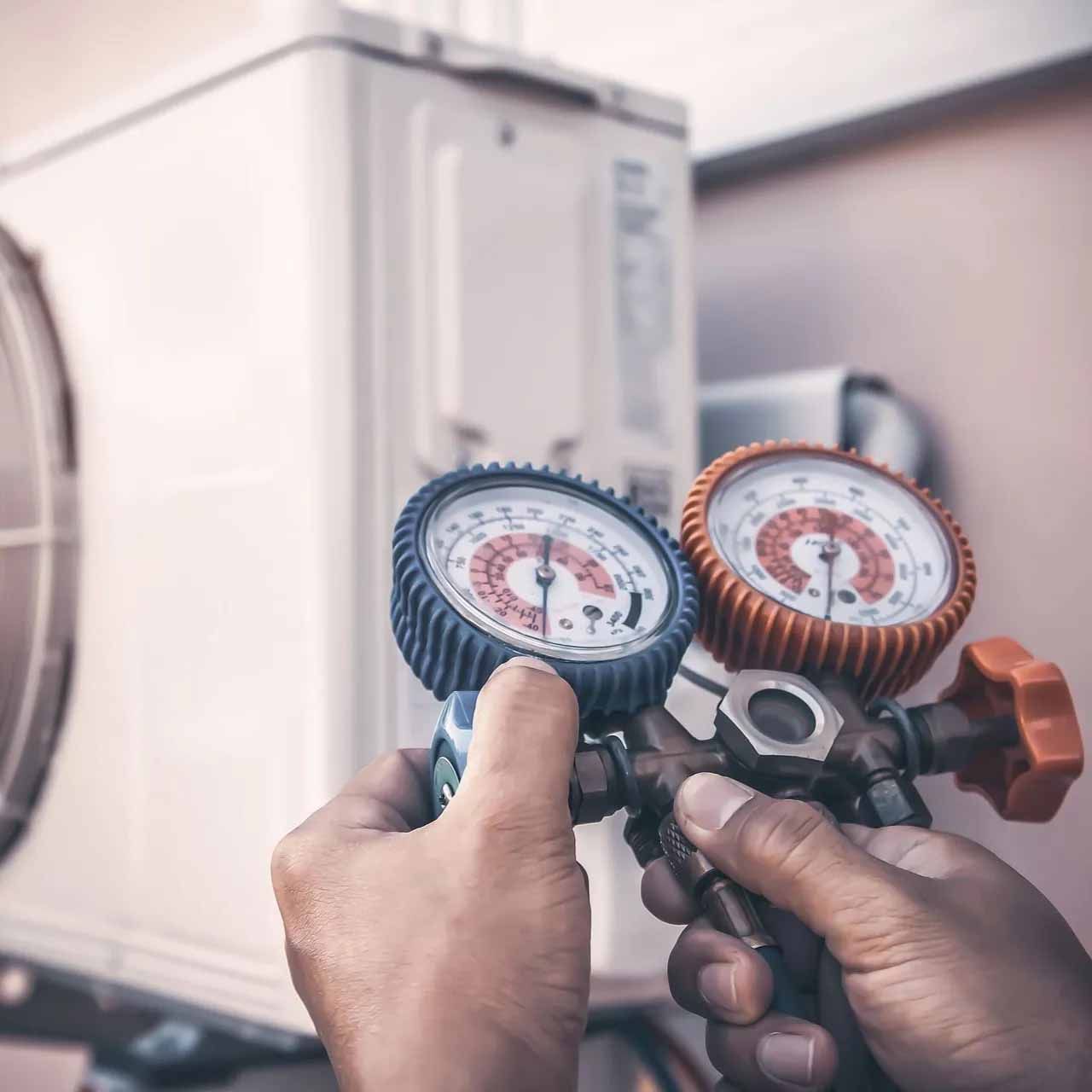 Les mains d'un technicien utilisant un manomètre pour vérifier la pression du réfrigérant sur une unité de climatisation extérieure.
