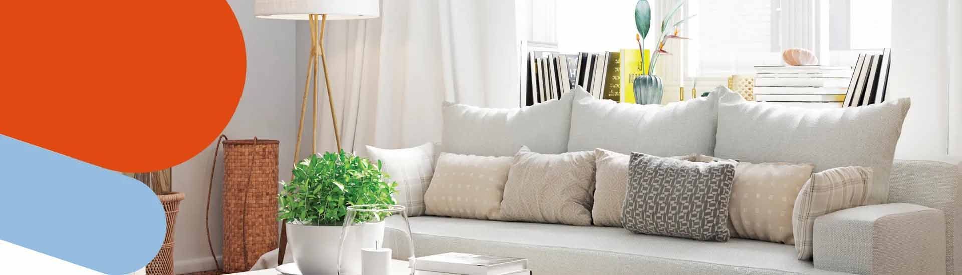 Un canapé clair agrémenté de divers coussins décoratifs, une plante verte en pot et un lampadaire dans un salon lumineux.