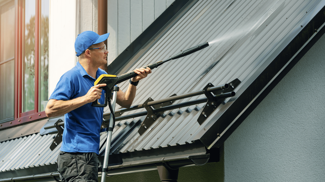 A man is cleaning the roof of a house with a high pressure washer.