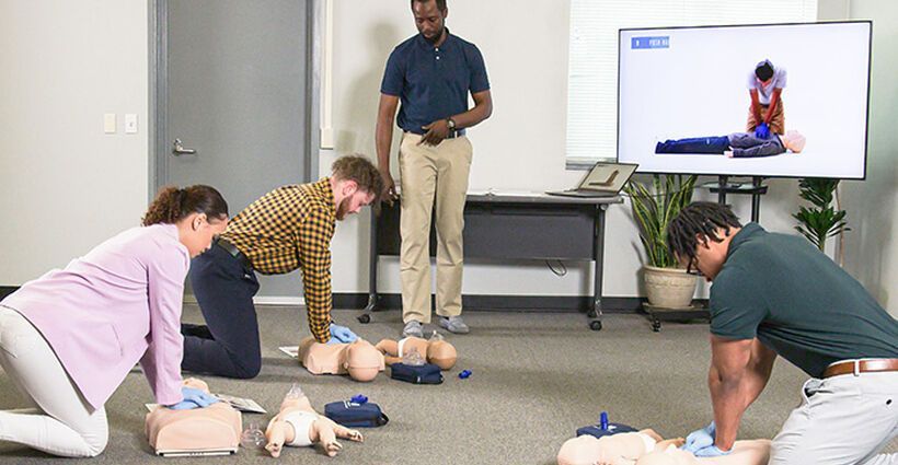 A group of people are practicing first aid in a room.