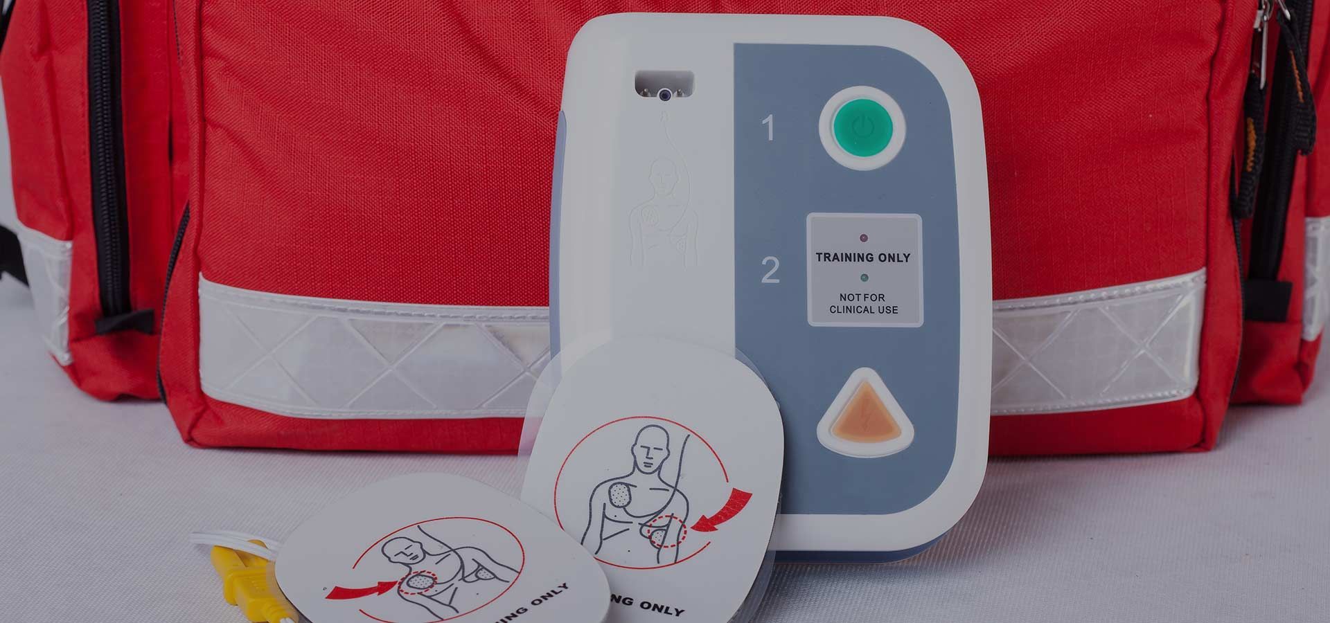 A defibrillator is sitting next to a red bag on a table.