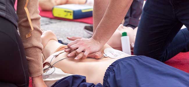 A group of people are practicing a defibrillator on a mannequin.