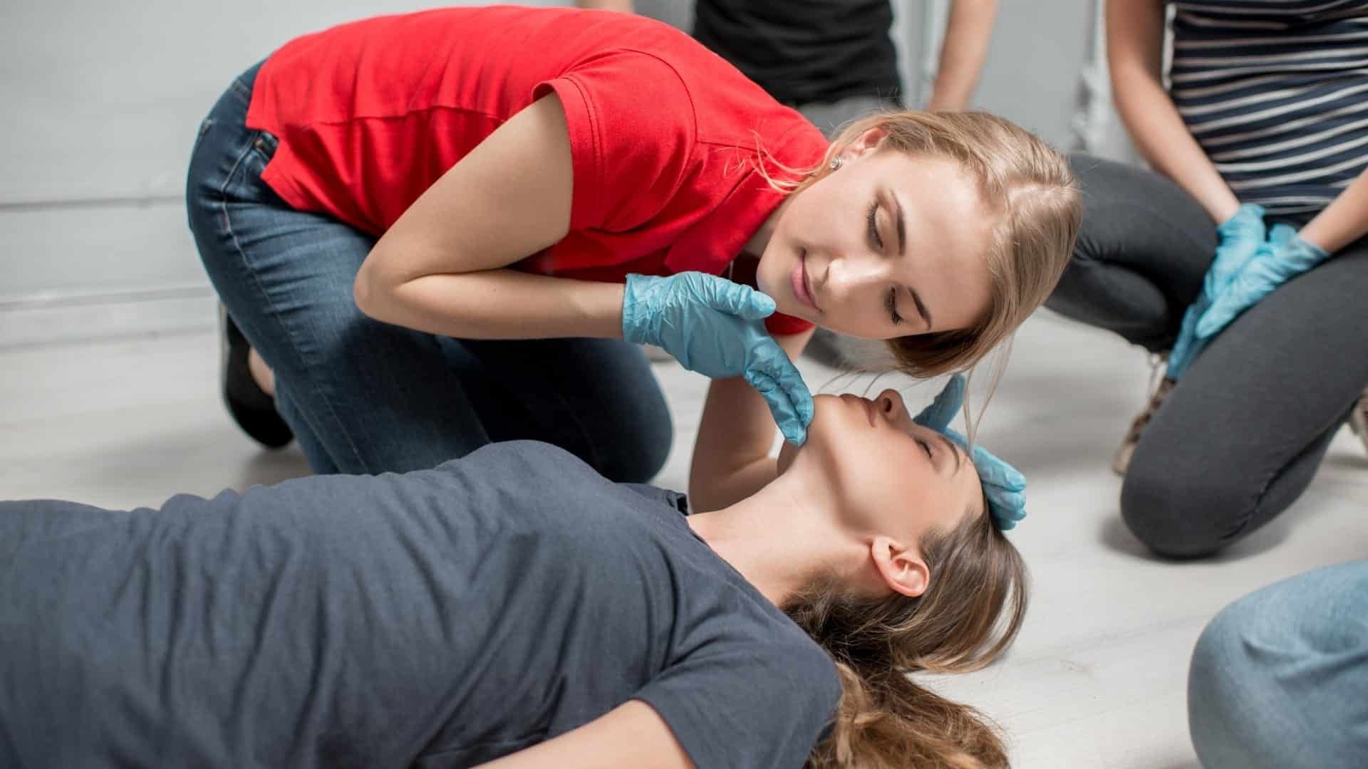 A woman is kneeling down next to a woman laying on the floor.