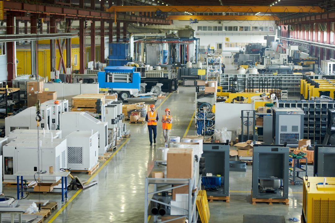 Large industrial factory floor with machinery, conveyors, and workers in orange safety vests.