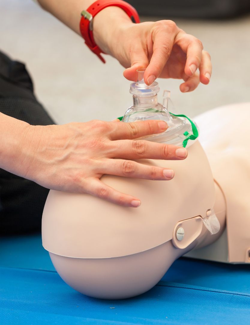 A person’s hands practice rescue breathing techniques on a medical CPR training mannequin using a clear face mask.