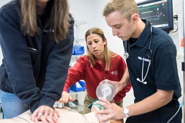 A group of people are standing around a mannequin in a hospital room.