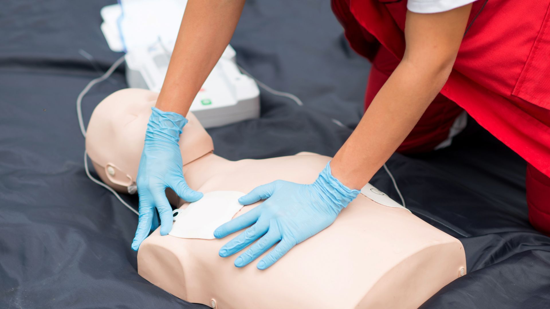 A person wearing blue gloves is doing a cpr on a mannequin.