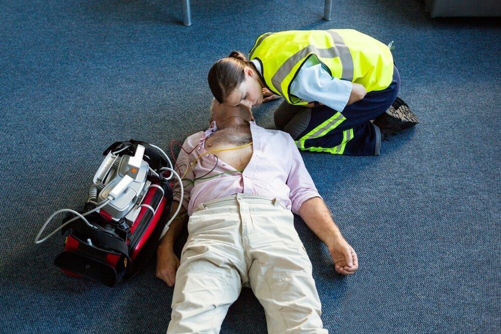 A woman is kneeling down next to a man laying on the floor.
