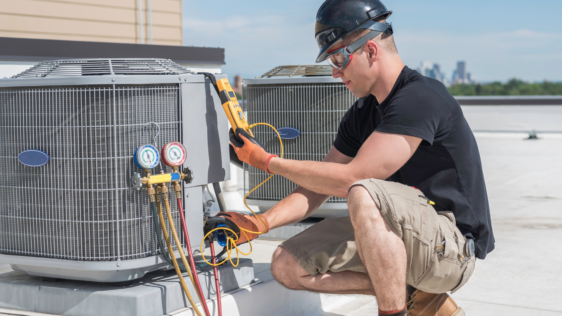 Technician using gauges on rooftop HVAC unit beside a black hard hat