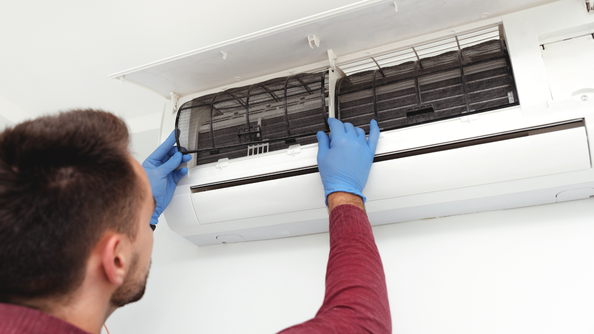 Technician cleaning an open wall-mounted air conditioner with blue gloves
