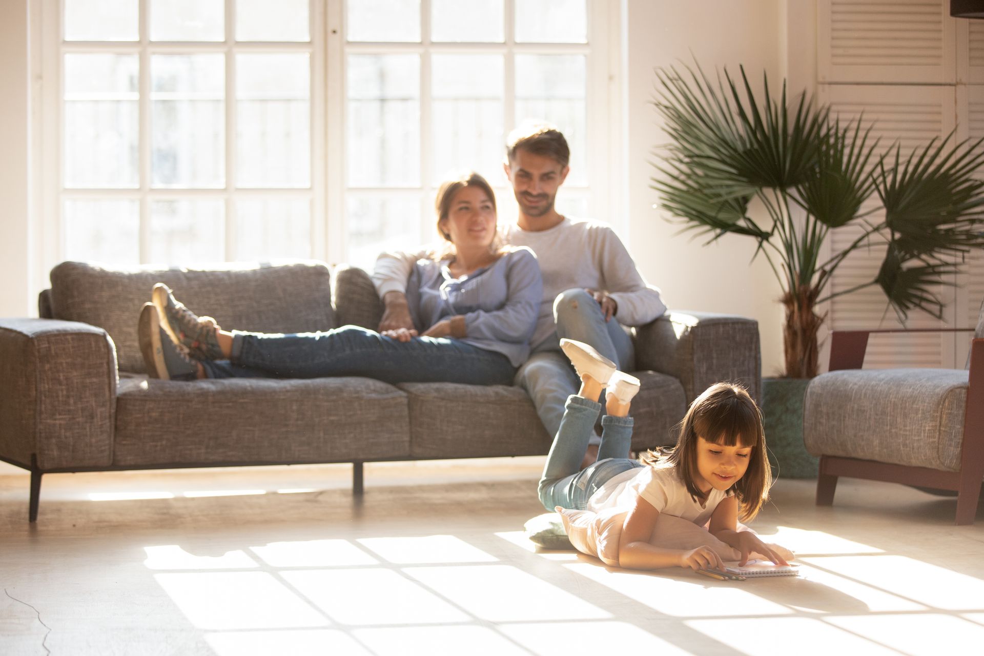 A family is sitting on a couch in a living room with a little girl laying on the floor.
