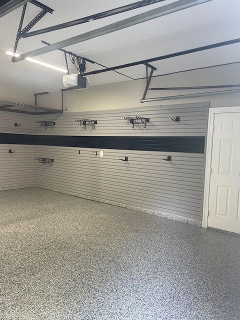 An organized garage interior featuring light gray slat walls with storage hooks, a black horizontal stripe, and epoxy floor.