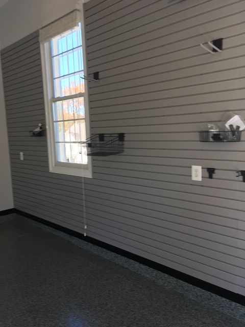 A grey slatted wall storage system in a garage with a window, several wire baskets, and hooks installed.