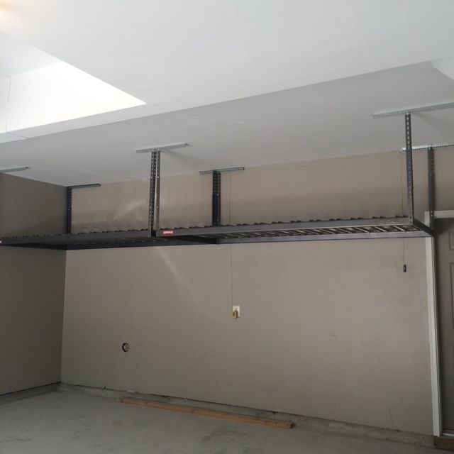 Two dark metal garage ceiling storage racks mounted to the white ceiling above a tan-walled space.