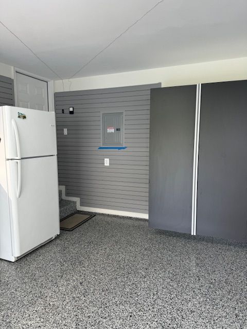 A garage interior with a white refrigerator, grey slat walls, a dark grey cabinet, and speckled epoxy flooring.