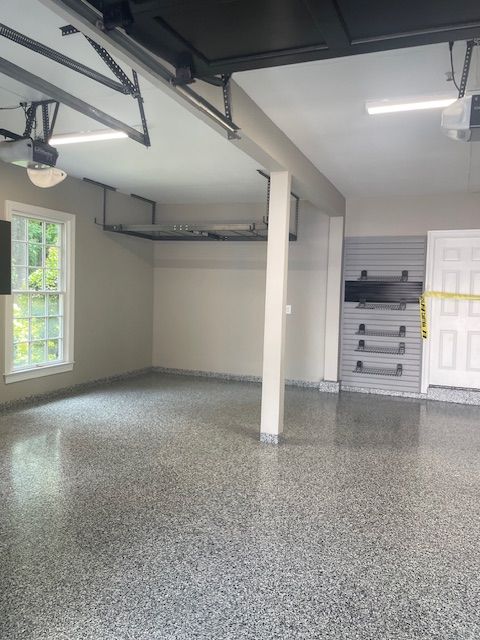 A bright, clean garage with light walls, a speckled epoxy floor, overhead storage, and gray wall-mounted storage panels.