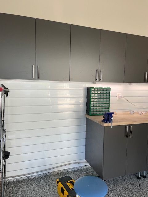 Garage workspace featuring gray wall cabinets, a light wood countertop, white horizontal slat walls, and a small bench vise.