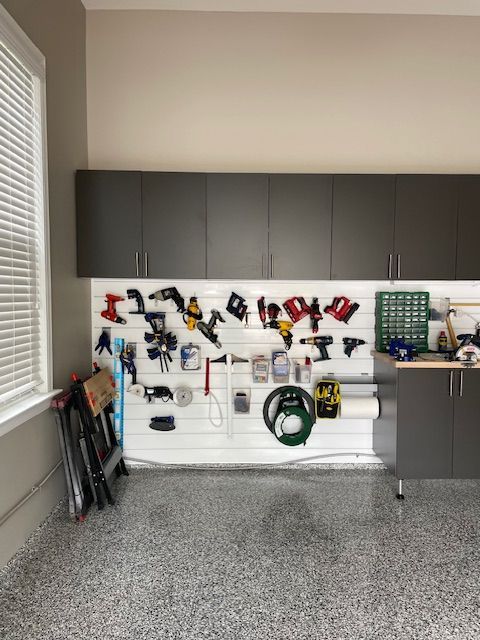 Garage wall with dark cabinets, a white slatwall organizer holding various power tools, and a speckled epoxy floor.