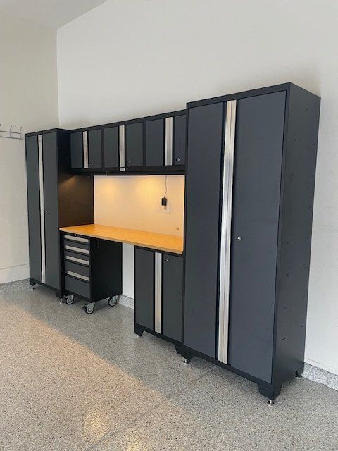 Dark gray modular garage storage cabinets with a wooden workbench and under-cabinet lighting on a speckled garage floor.