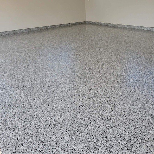 A gray, speckled epoxy floor inside a garage with clean, neutral-colored walls.