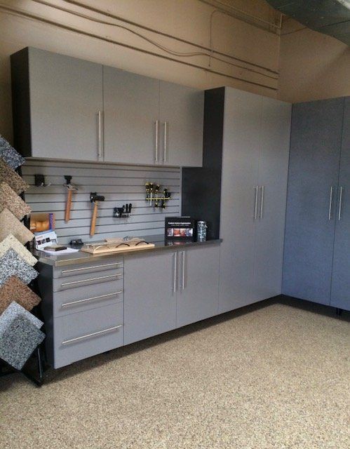 Gray garage storage cabinets and lockers with a slat wall organizing tools, set against a speckled epoxy floor.
