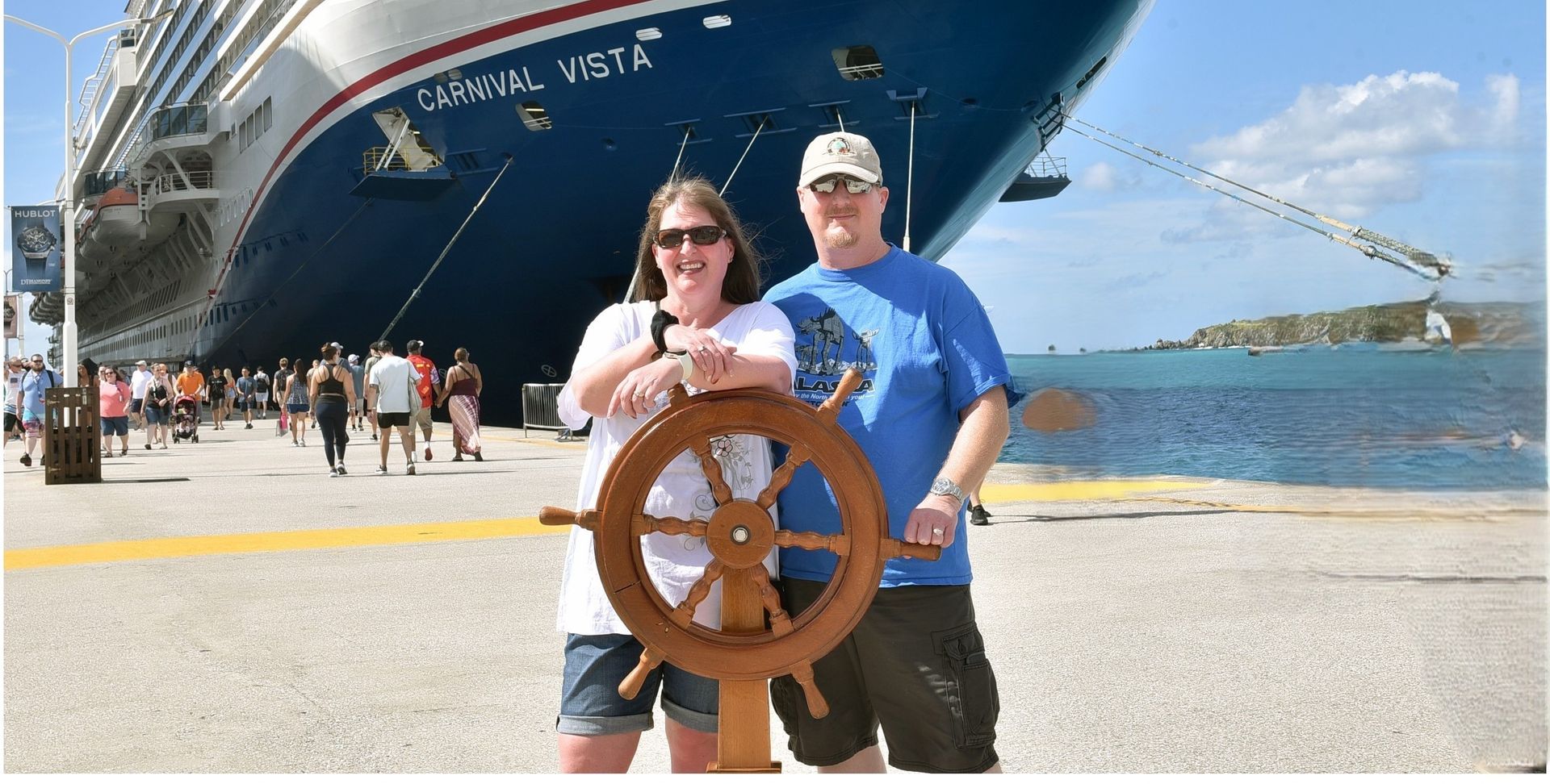 Couple poses with ship's wheel on dock in front of Carnival Vista cruise ship.