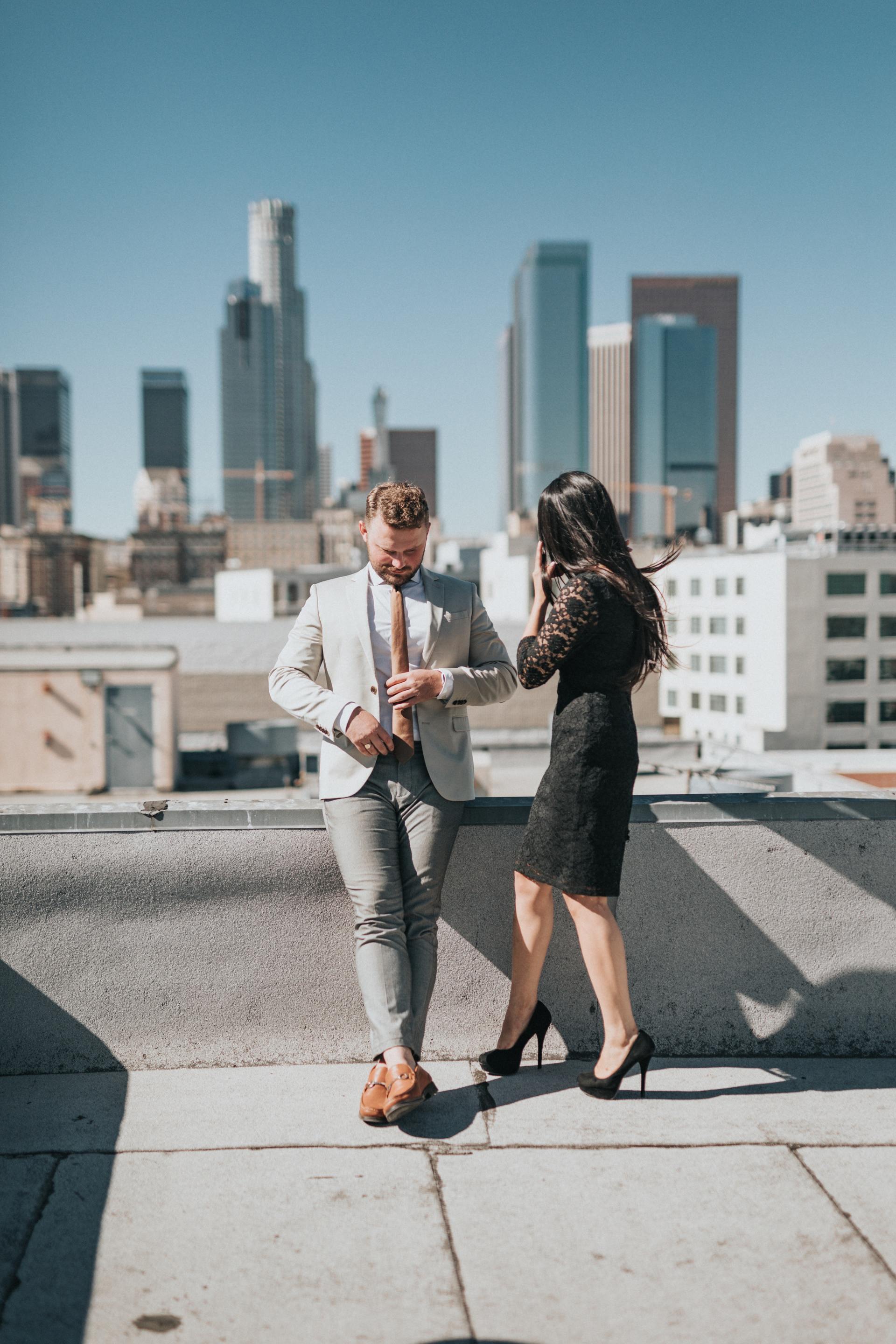 A man and a woman are standing on a rooftop in front of a city skyline.