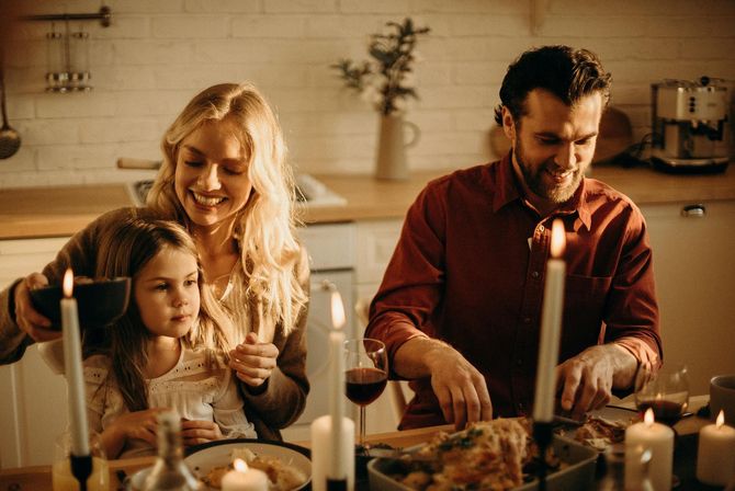 Family preparing food together in a warm kitchen, with candles lit on the counter.