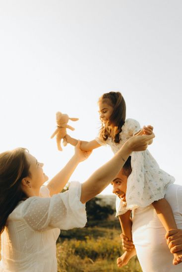 Woman lifting a smiling child in a white dress outdoors against a bright sky