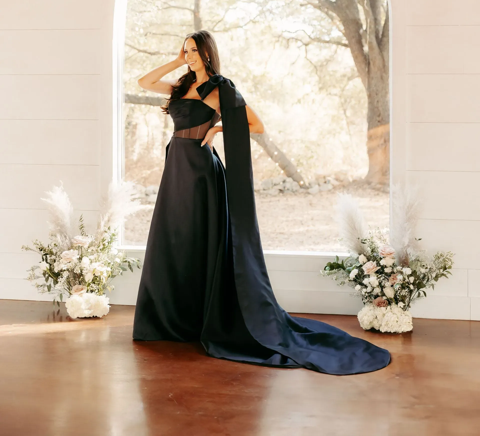 A woman in a black dress is standing in front of a window.