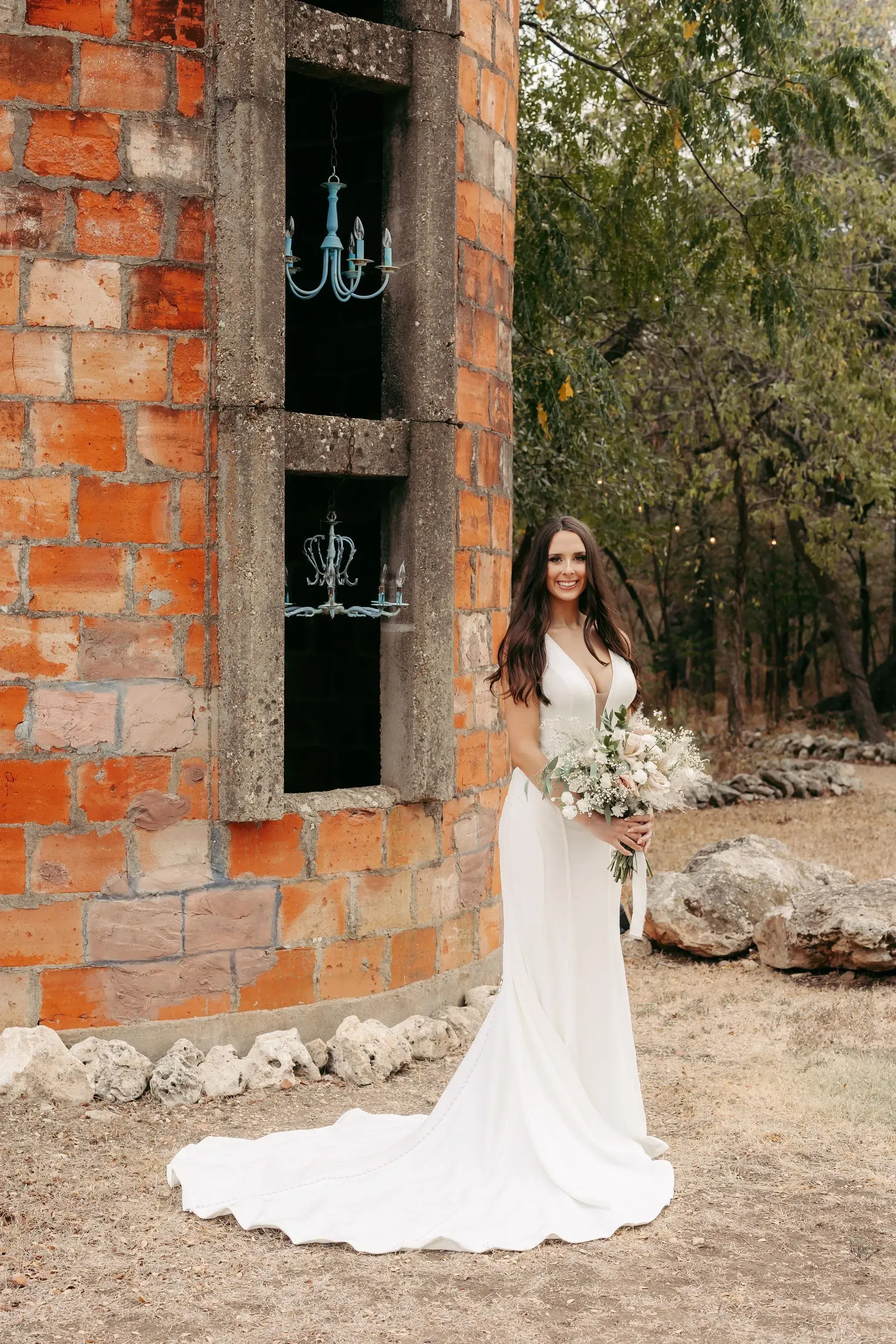 A bride in a white dress is standing in front of a brick building holding a bouquet of flowers.