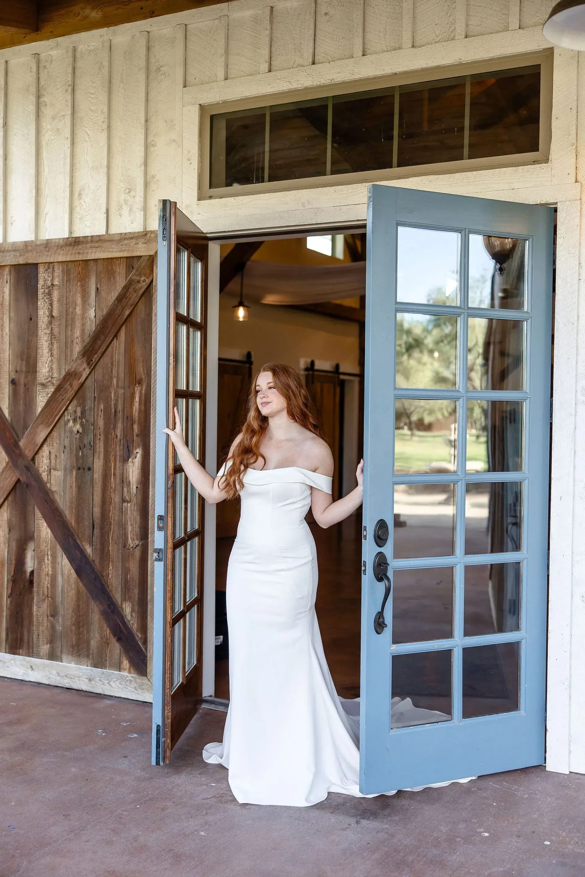 A woman in a wedding dress is standing in front of a barn door.