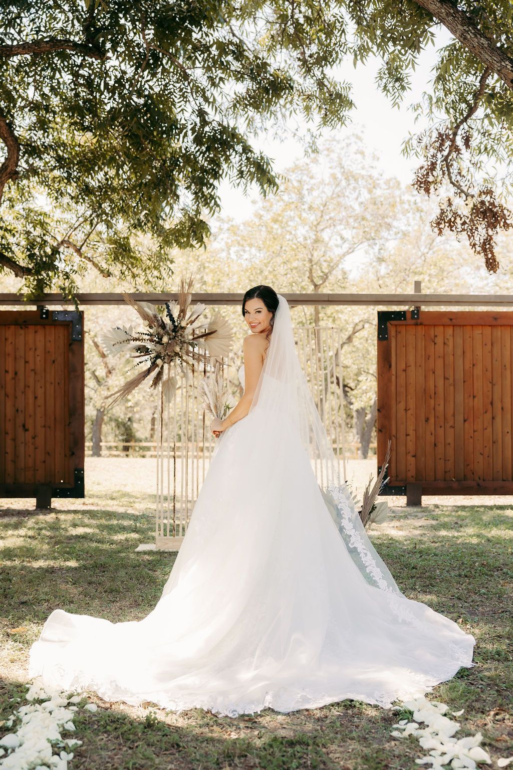 A bride in a wedding dress and veil is standing in the grass.