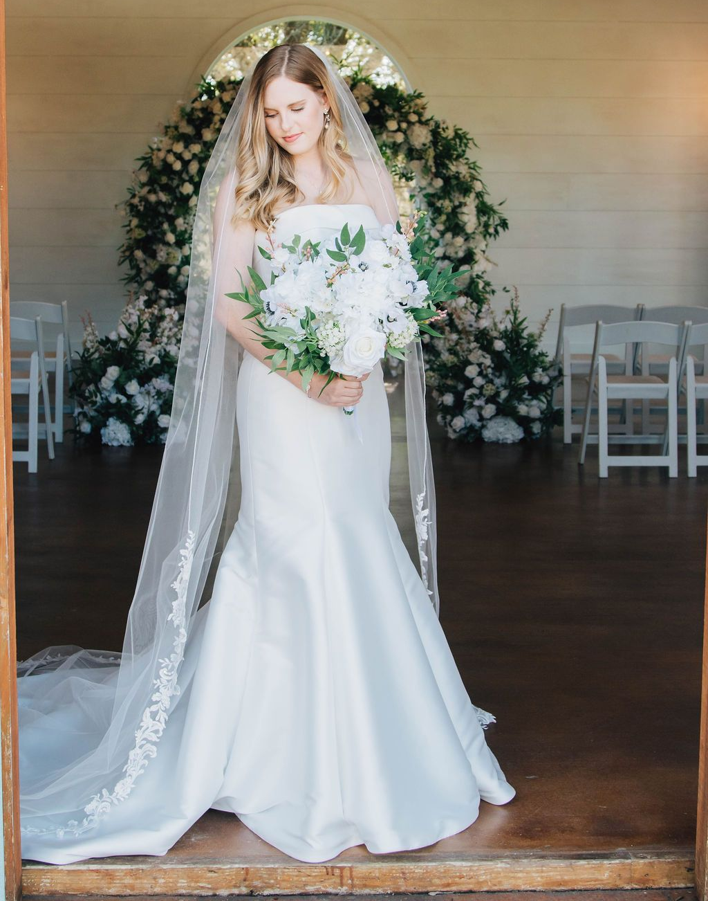 The bride is wearing a long veil and holding a bouquet of flowers.
