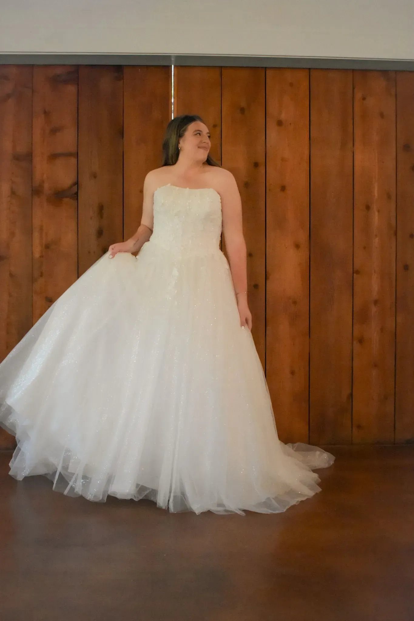 A woman in a white wedding dress is standing in front of a wooden wall.