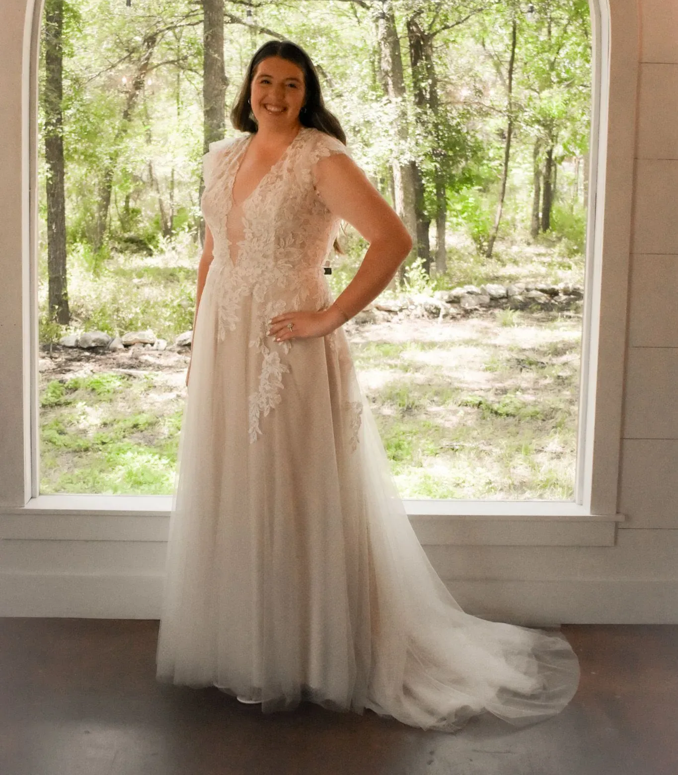 A woman in a wedding dress is standing in front of a window.