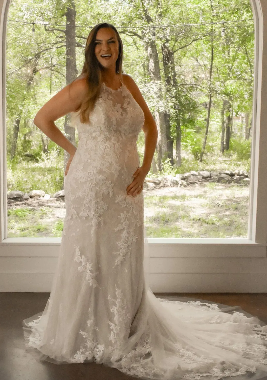 A woman in a wedding dress is standing in front of a window.