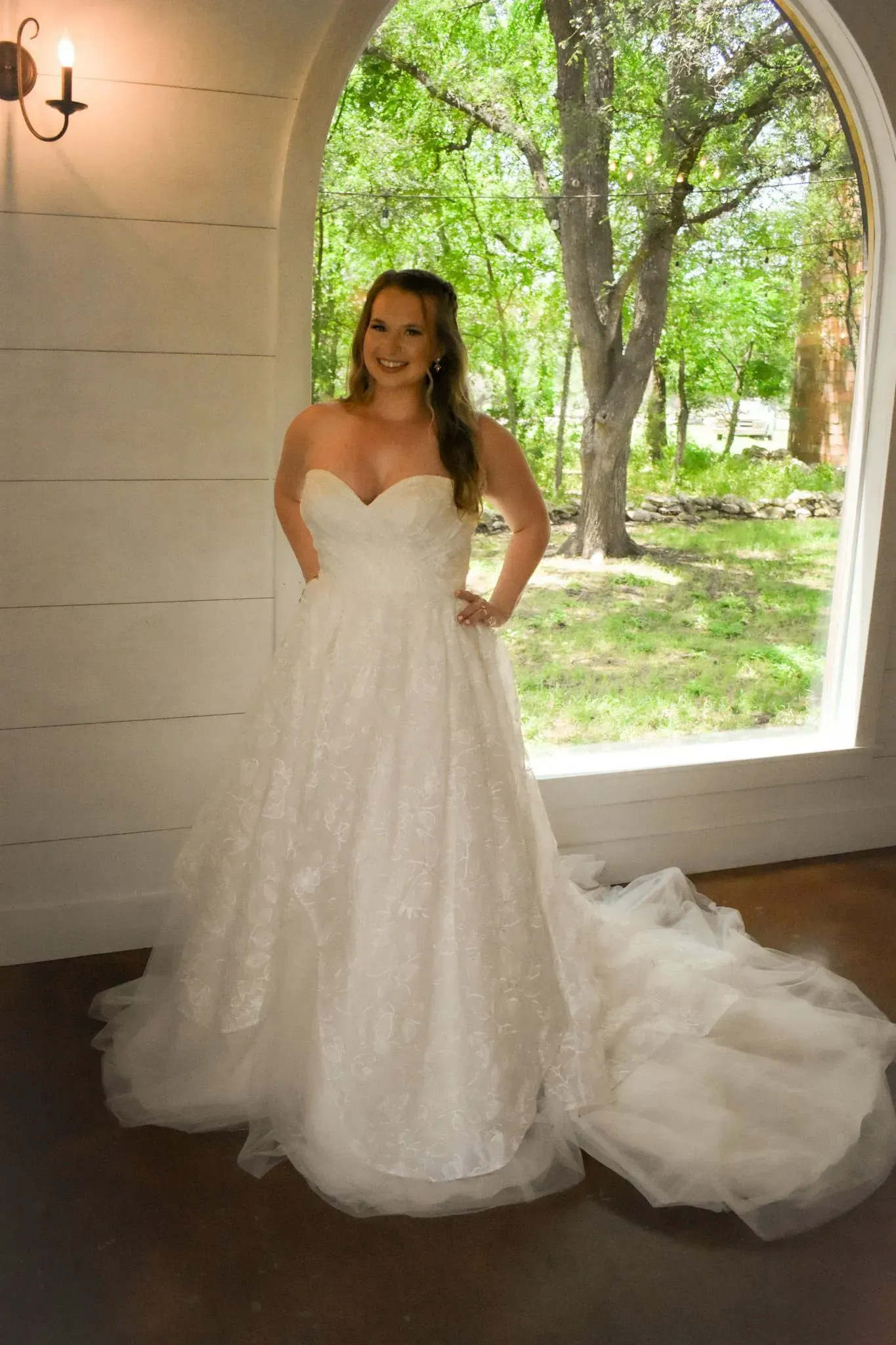 A woman in a wedding dress is standing in front of a window.