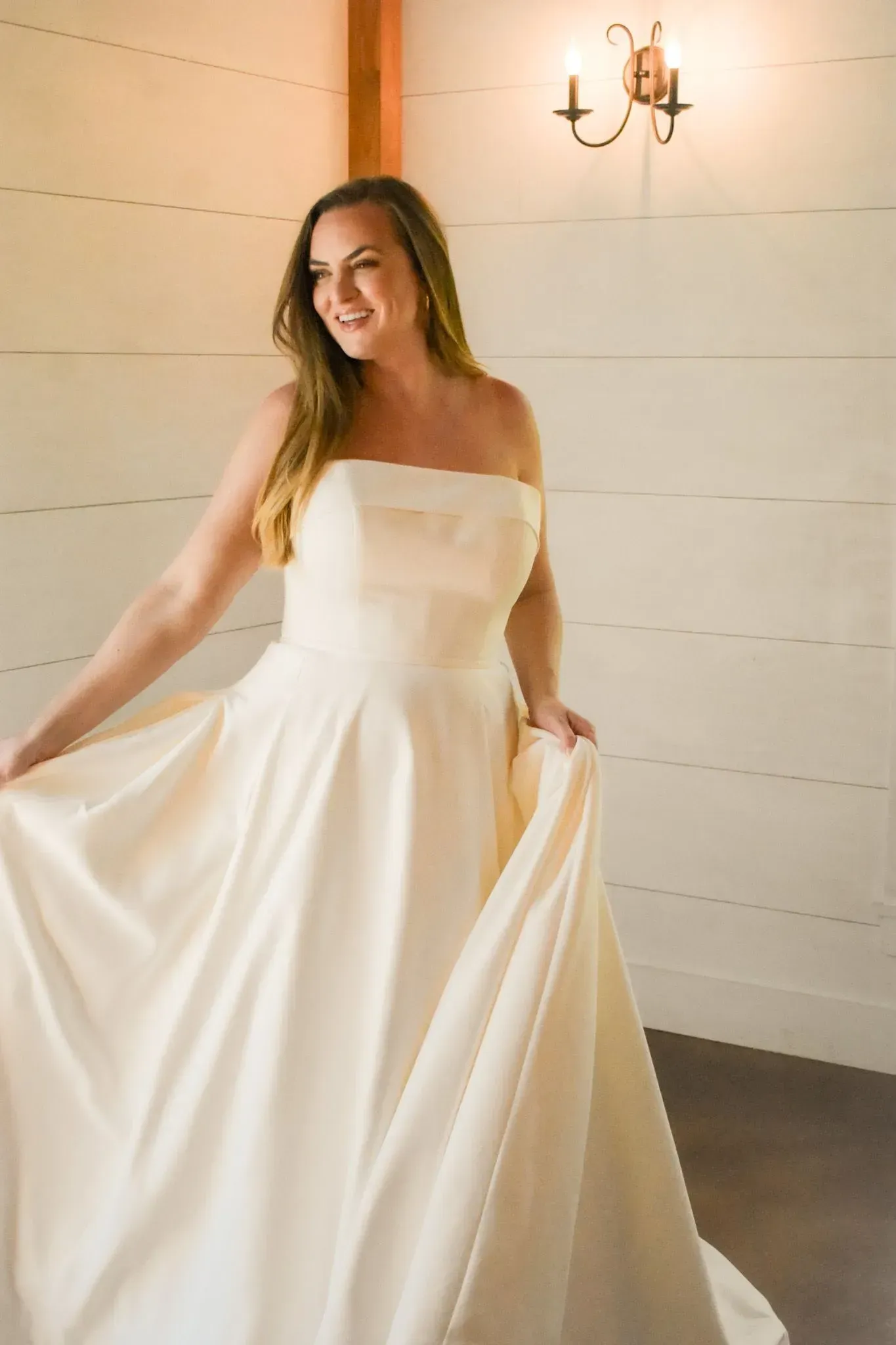 A woman in a white wedding dress is standing in front of a white wall.
