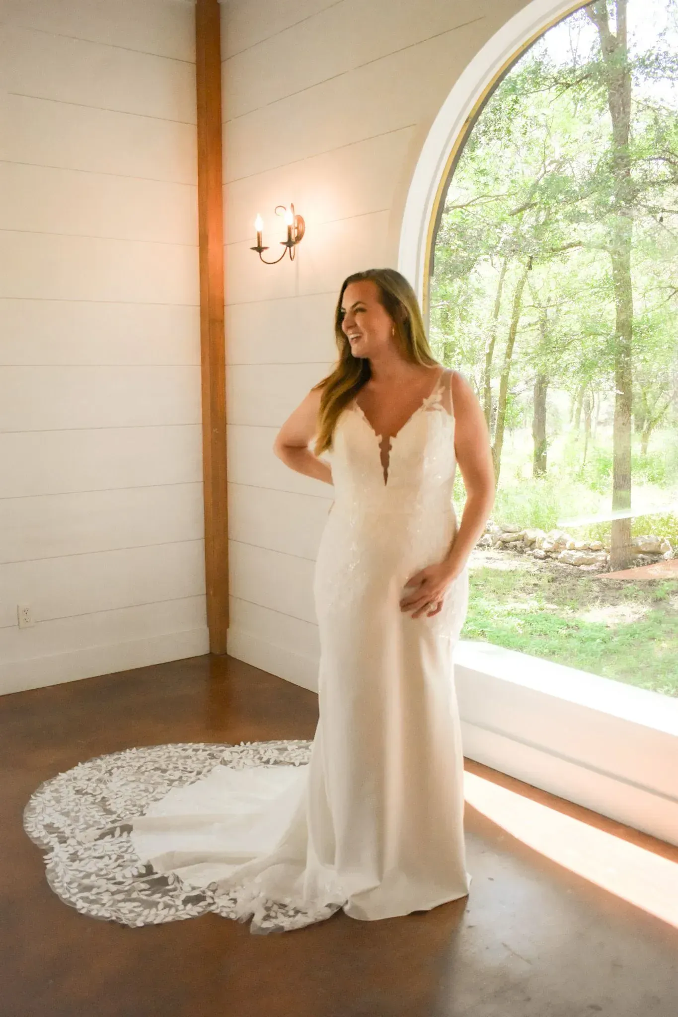 A woman in a wedding dress is standing in front of a window.