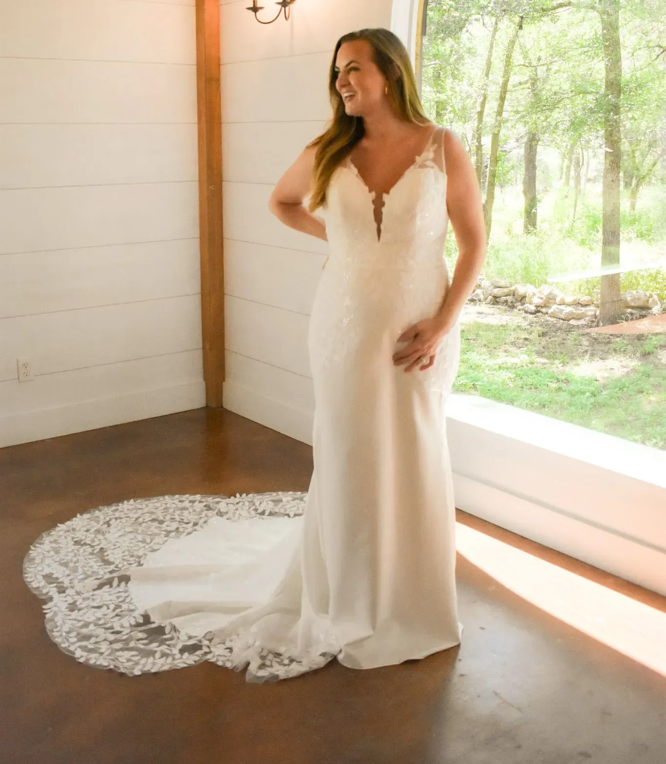 A woman in a wedding dress is standing in front of a window.