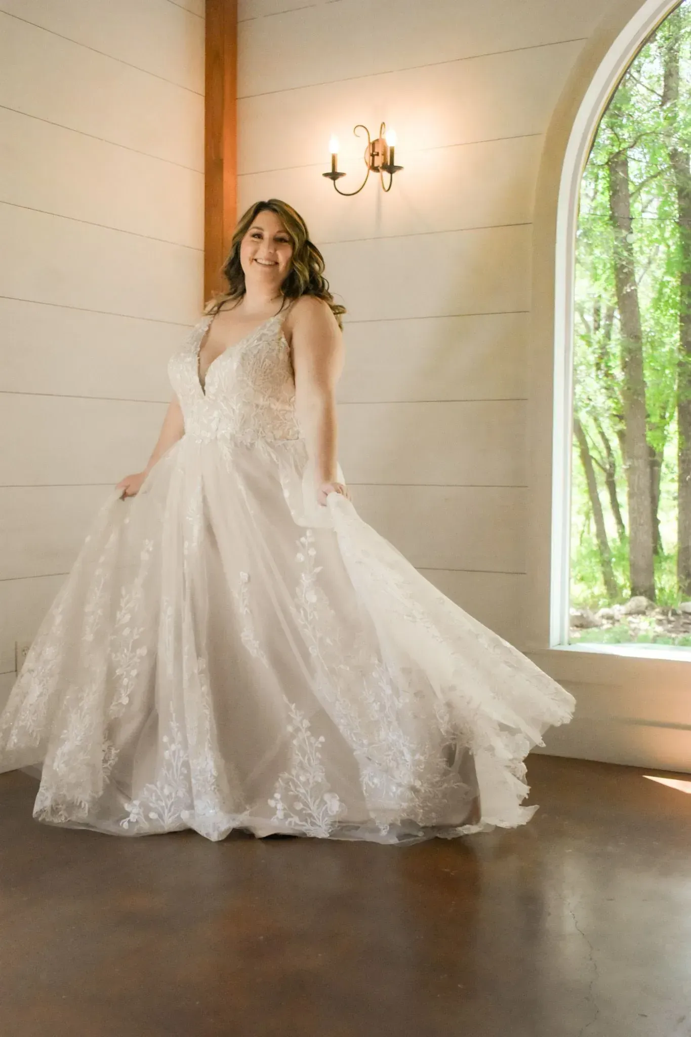A woman in a wedding dress is standing in front of a window.