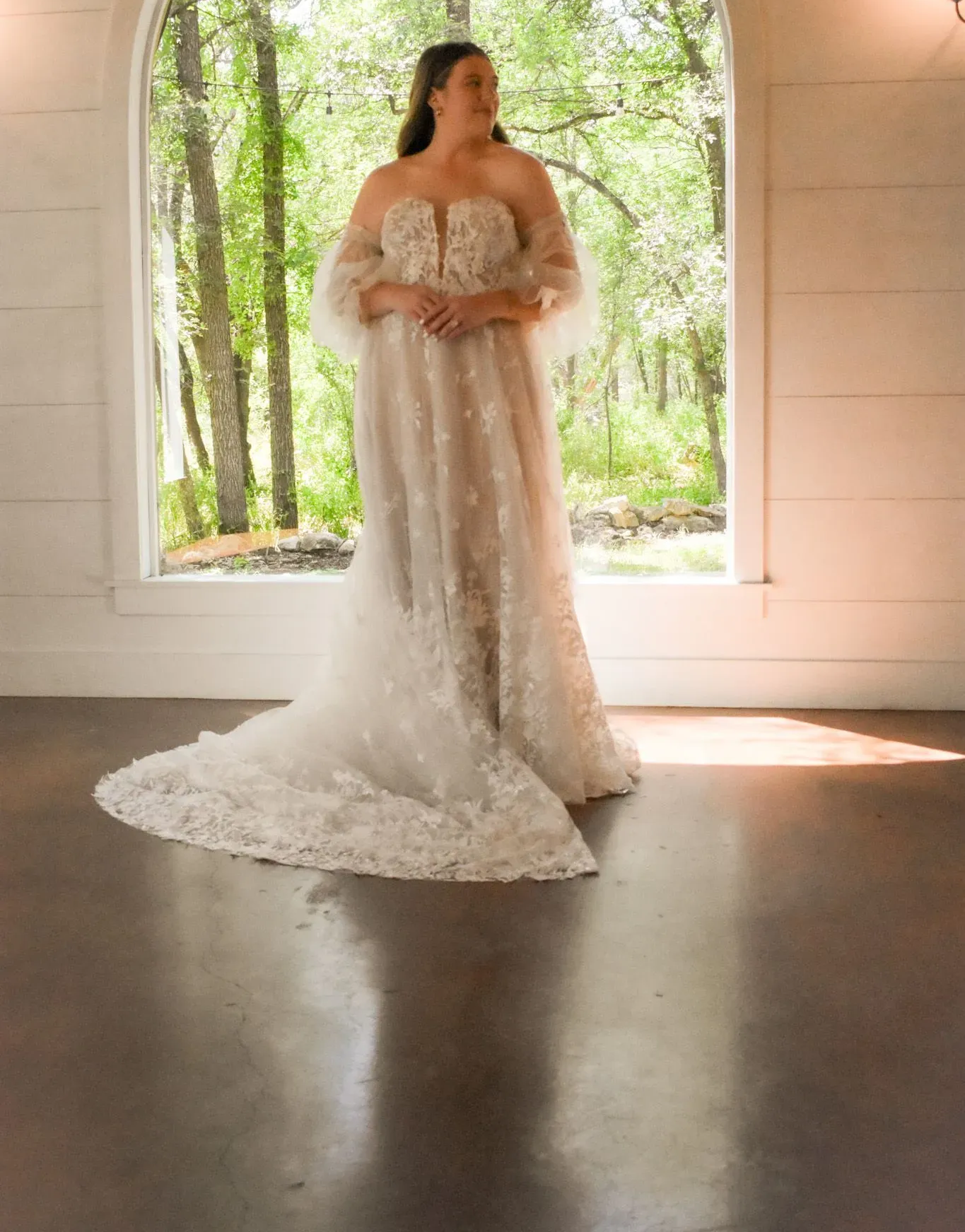A woman in a wedding dress is standing in front of a window.