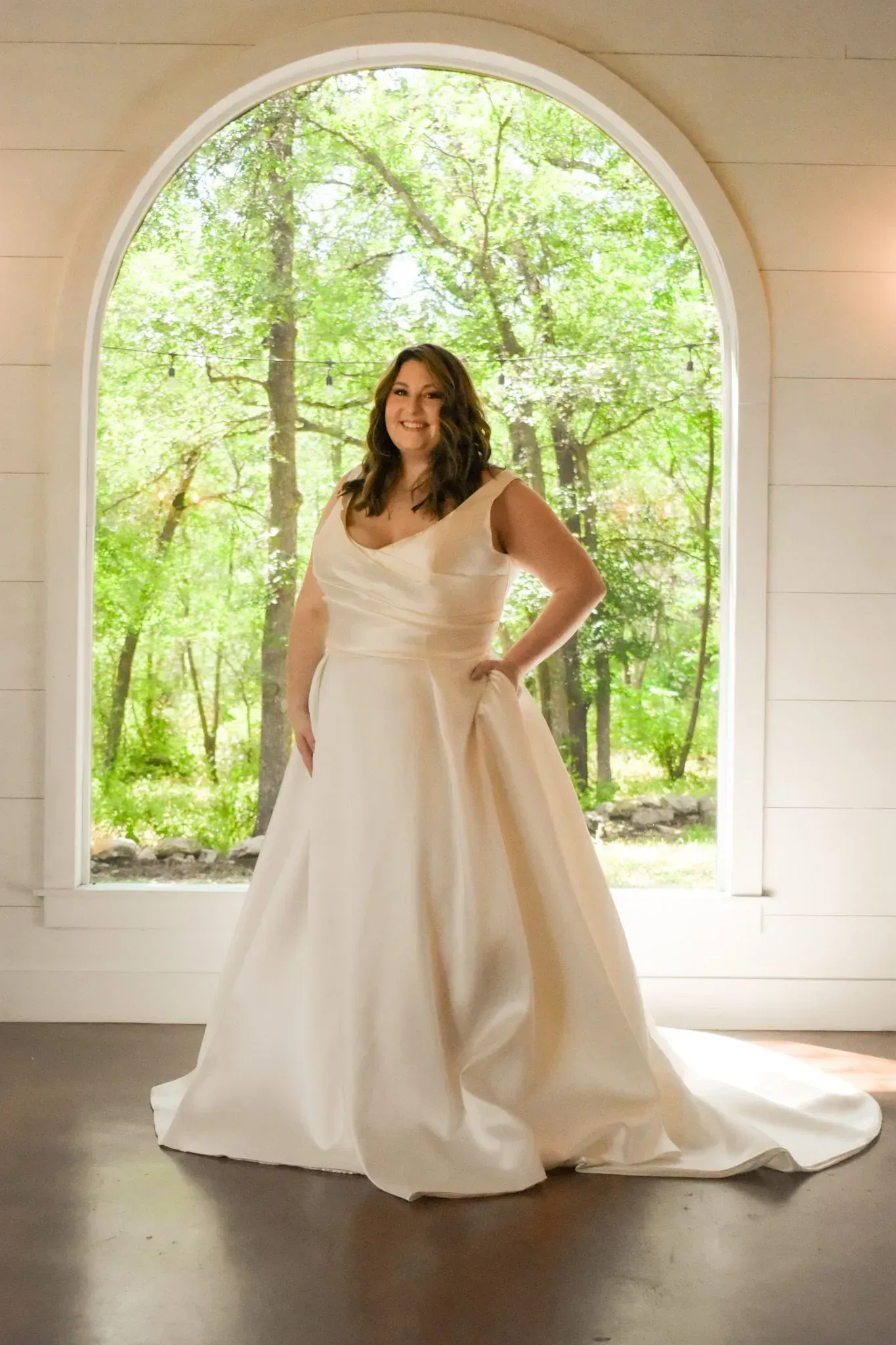 A woman in a white wedding dress is standing in front of a window.