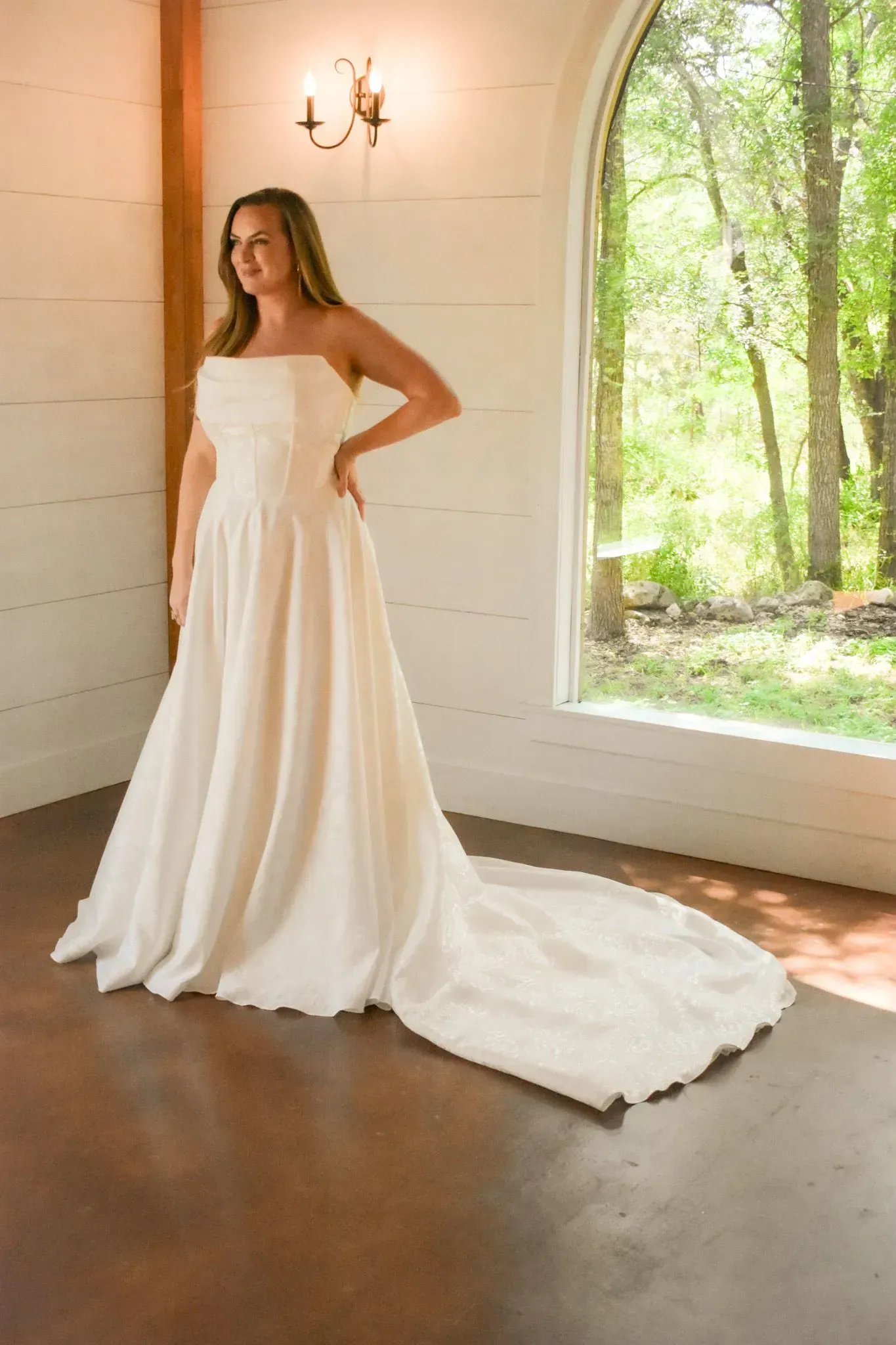 A woman in a white wedding dress is standing in front of a window.