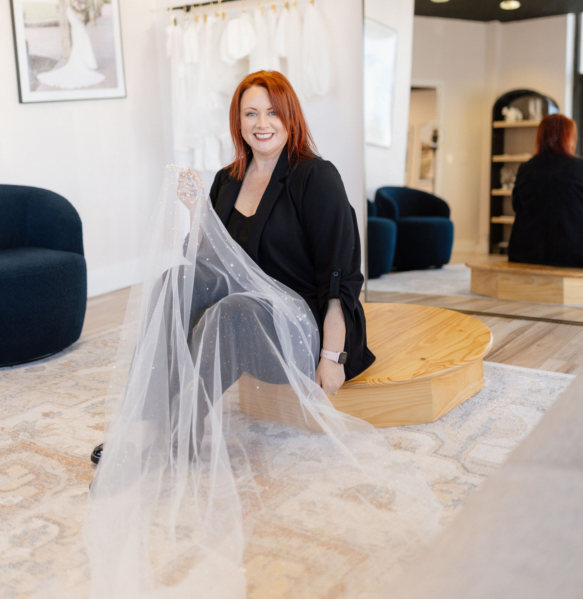 Two women are standing next to each other in front of a wall of wedding dresses.
