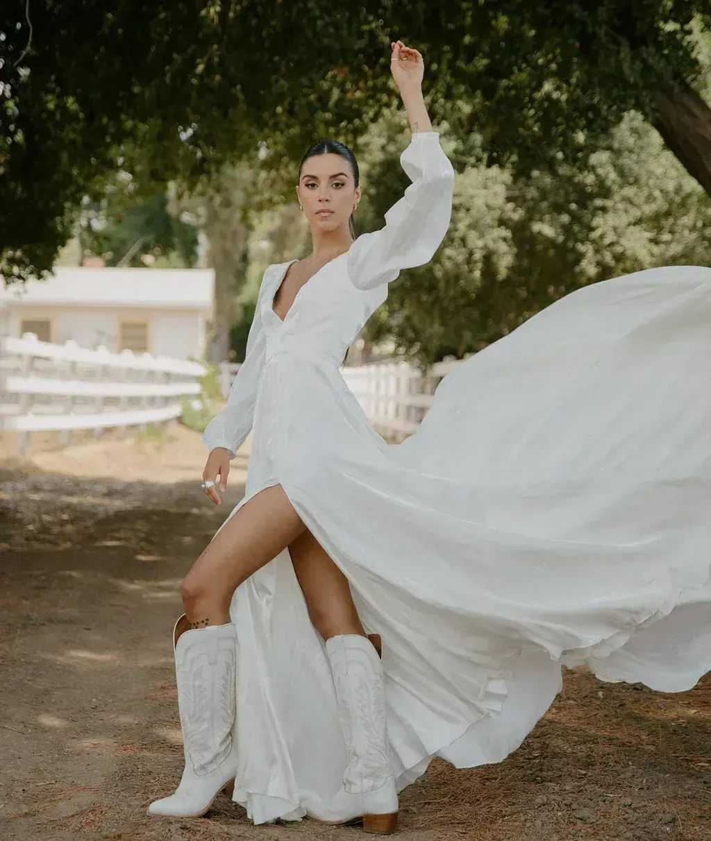 A woman in a white dress and cowboy boots is standing in a field.